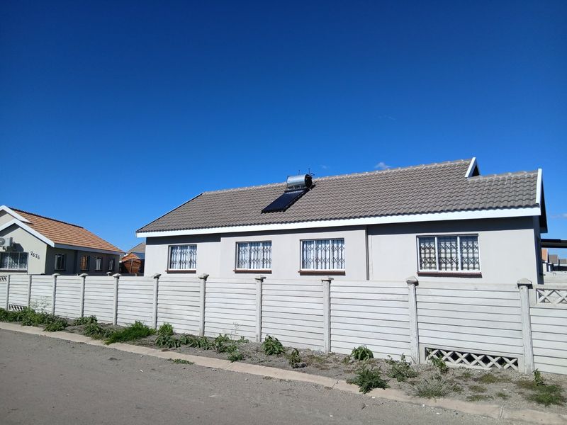 Front exterior view of a single-story house featuring a concrete tile roof, solar water heating system, and a secure precast concrete boundary wall.