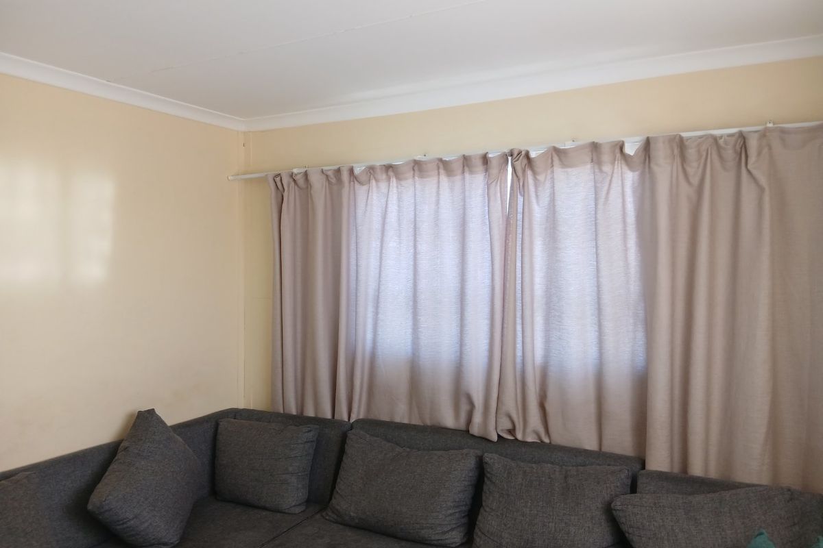 A living room area featuring neutral wall paint, coving, and a window fitted with a curtain rod.