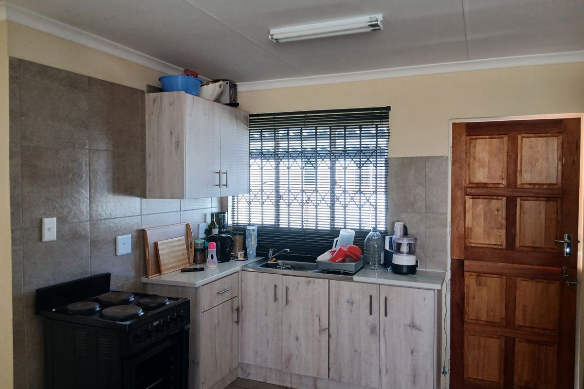 A functional kitchen featuring laminate cabinetry, tiled splashbacks, a stainless steel sink, and a freestanding electric stove with a timber door entrance.