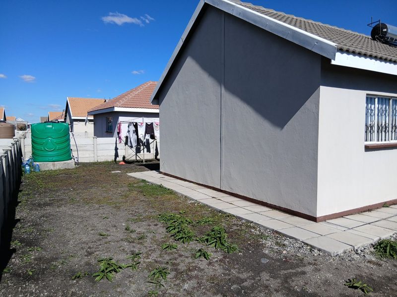 Rear view of the property featuring a concrete paved walkway, a water tank, and a solar geyser installed on the tiled roof.