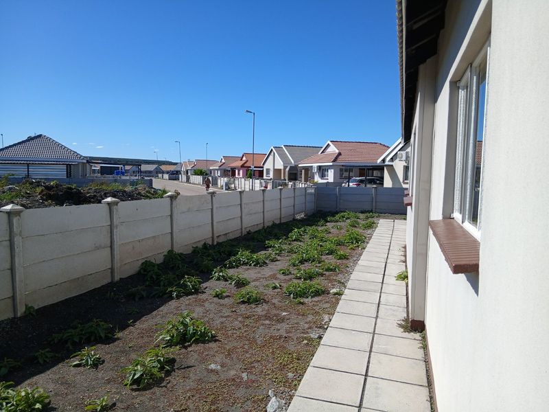 Side exterior view of the property featuring a paved walkway, precast concrete boundary wall, and an unlandscaped garden area.