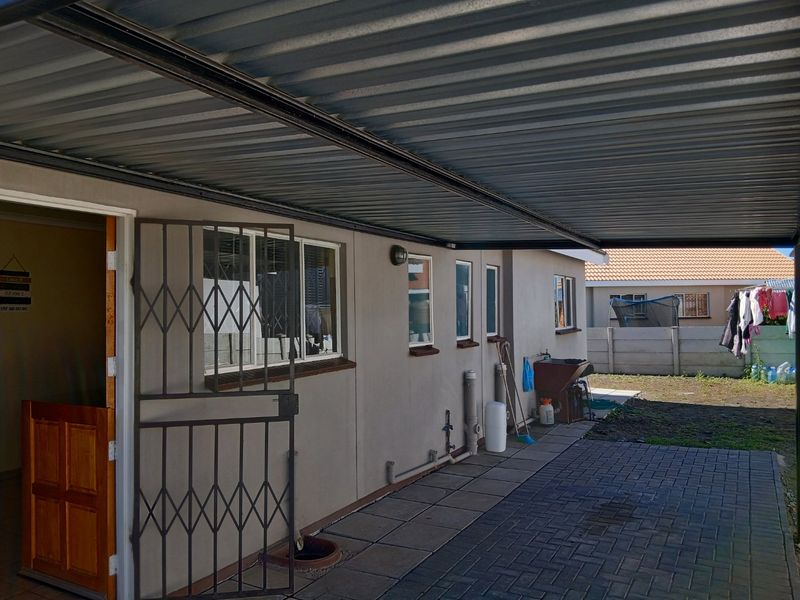 A covered outdoor patio area featuring paved flooring, a corrugated metal roof, and a security gate, providing a functional transition space to the rear garden.