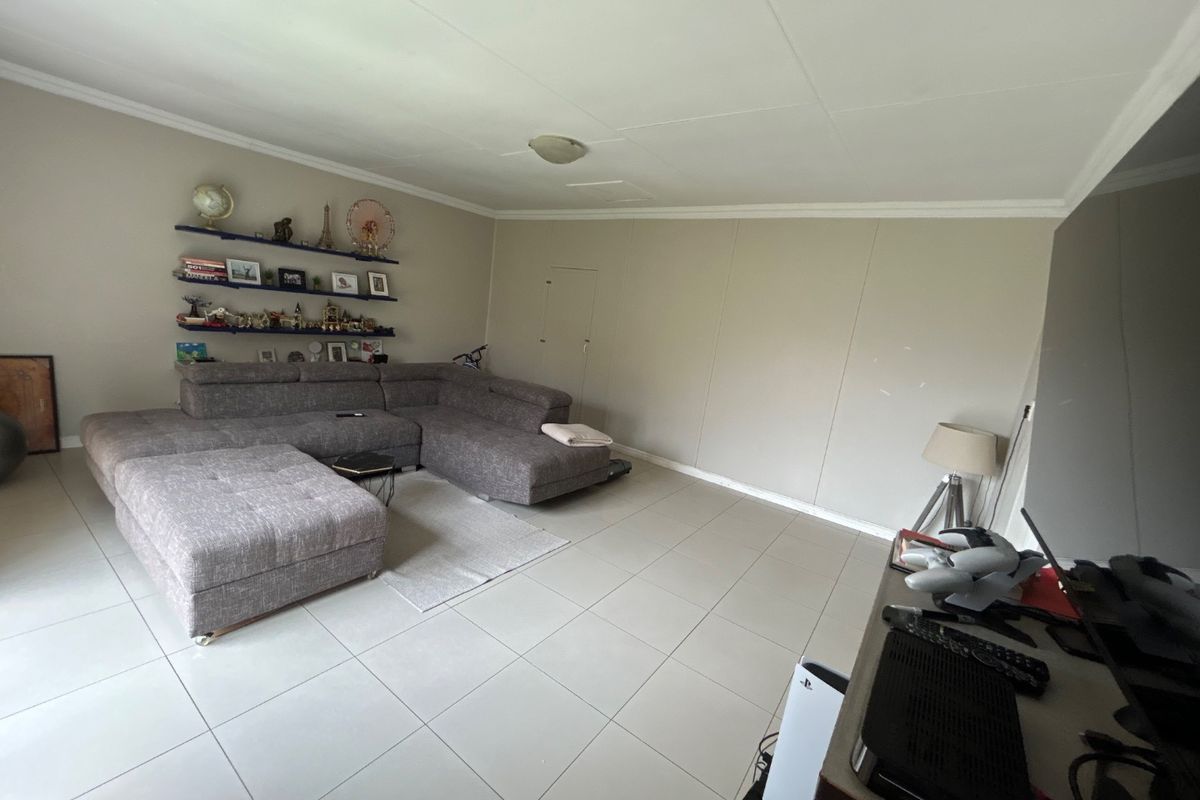 A spacious living room featuring neutral tiled flooring, coved ceiling cornices, and a functional layout suitable for comfortable family seating.