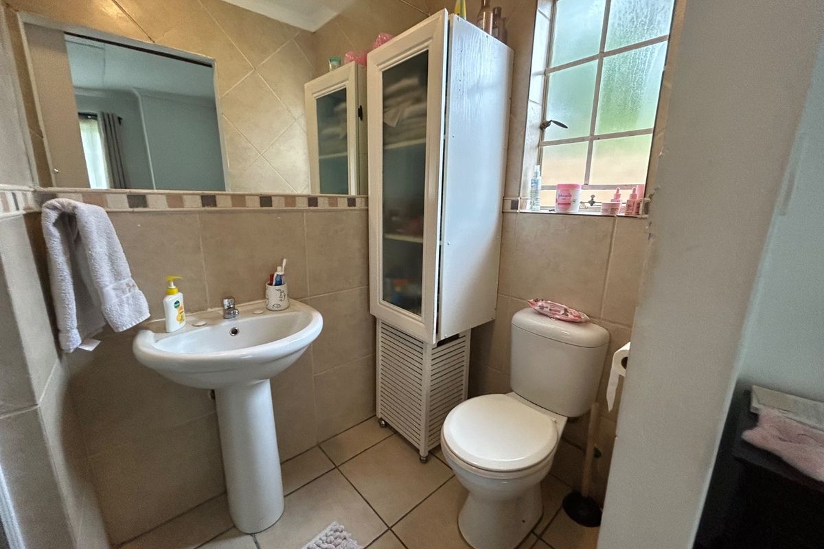 A functional bathroom featuring a pedestal basin, toilet, tiled finishes, and a wall-mounted mirror, providing a practical layout for daily use.
