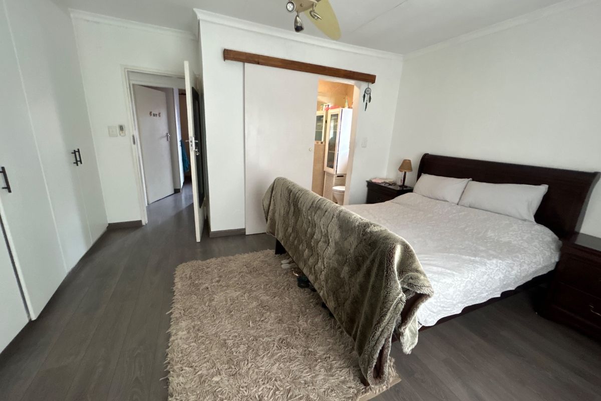Spacious bedroom featuring laminate flooring, built-in cupboards, and a ceiling fan, with an adjoining en-suite bathroom accessed via a sliding door.