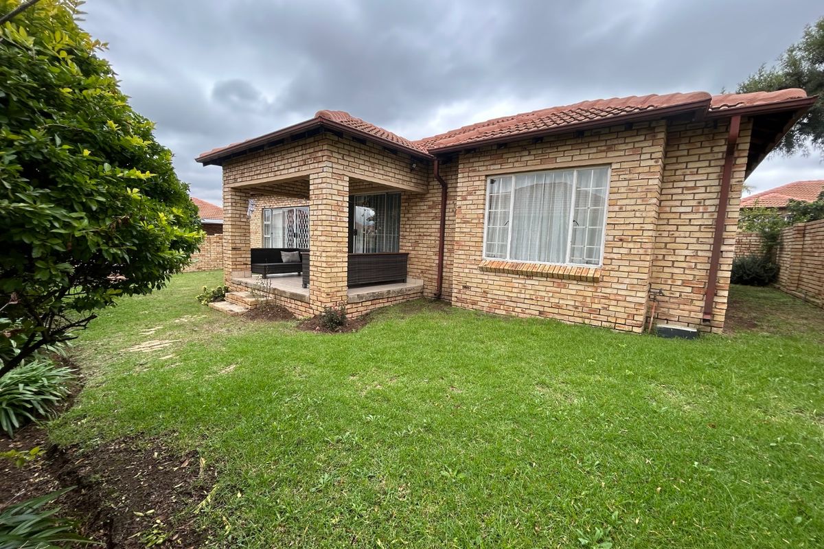 Rear view of a face brick townhouse featuring a covered patio area and a well-maintained lawn under a cloudy sky.