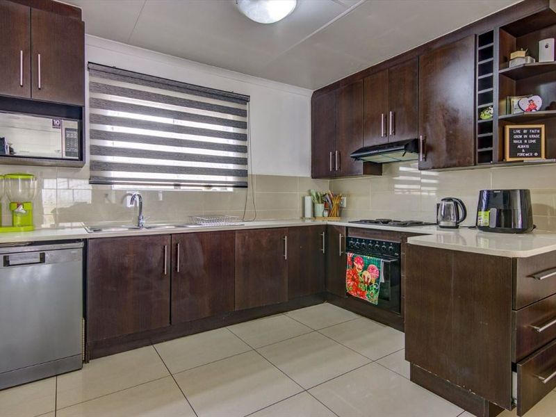 A functional kitchen featuring dark wood cabinetry, stone countertops, a built-in oven with gas hob, and tiled flooring with a neutral backsplash.