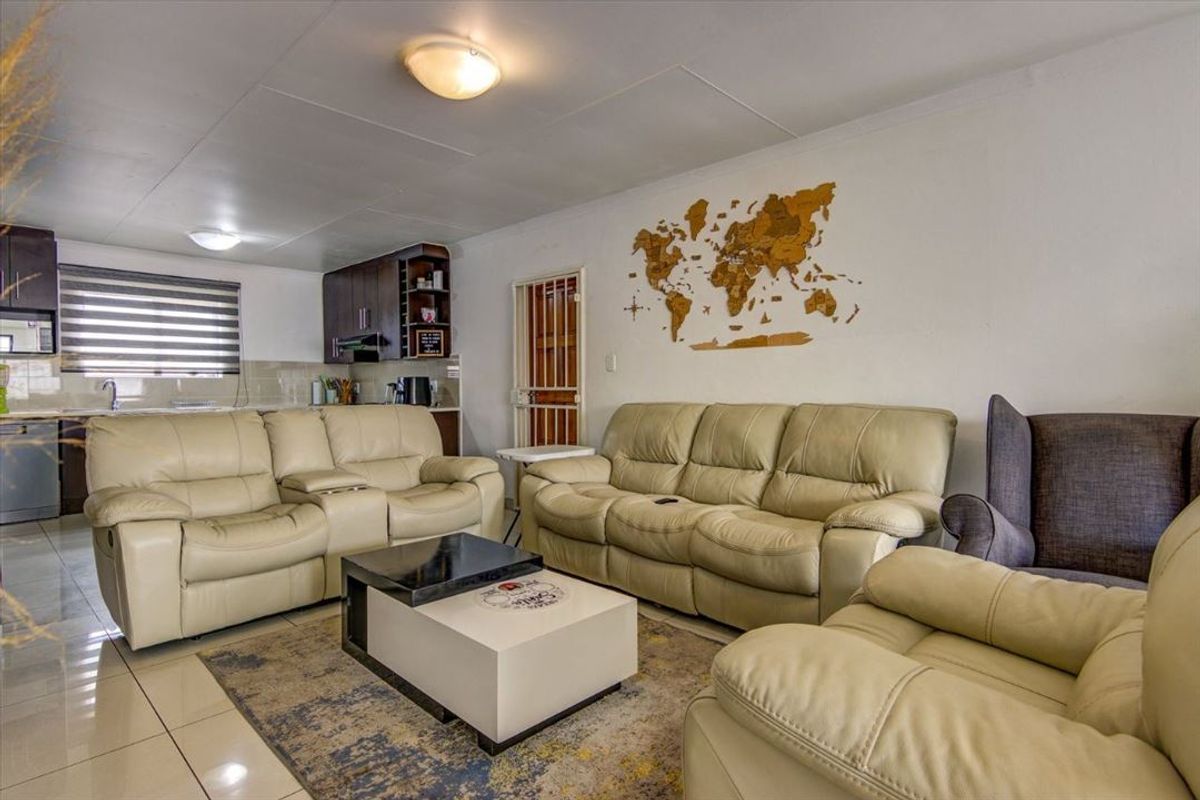 Open-plan living area featuring tiled flooring, integrated kitchen cabinetry, and a security gate, providing a functional and connected layout.