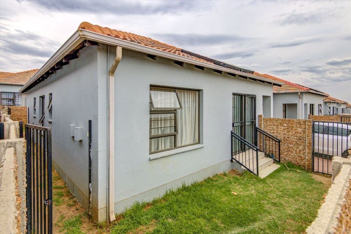 Rear view of the townhouse featuring a tiled roof, aluminium window frames, security gate access, and a private garden area with boundary walling.