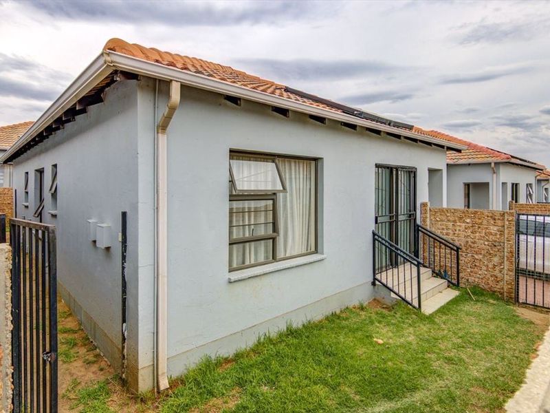 Rear view of the townhouse featuring a tiled roof, aluminium window frames, security gate access, and a private garden area with boundary walling.