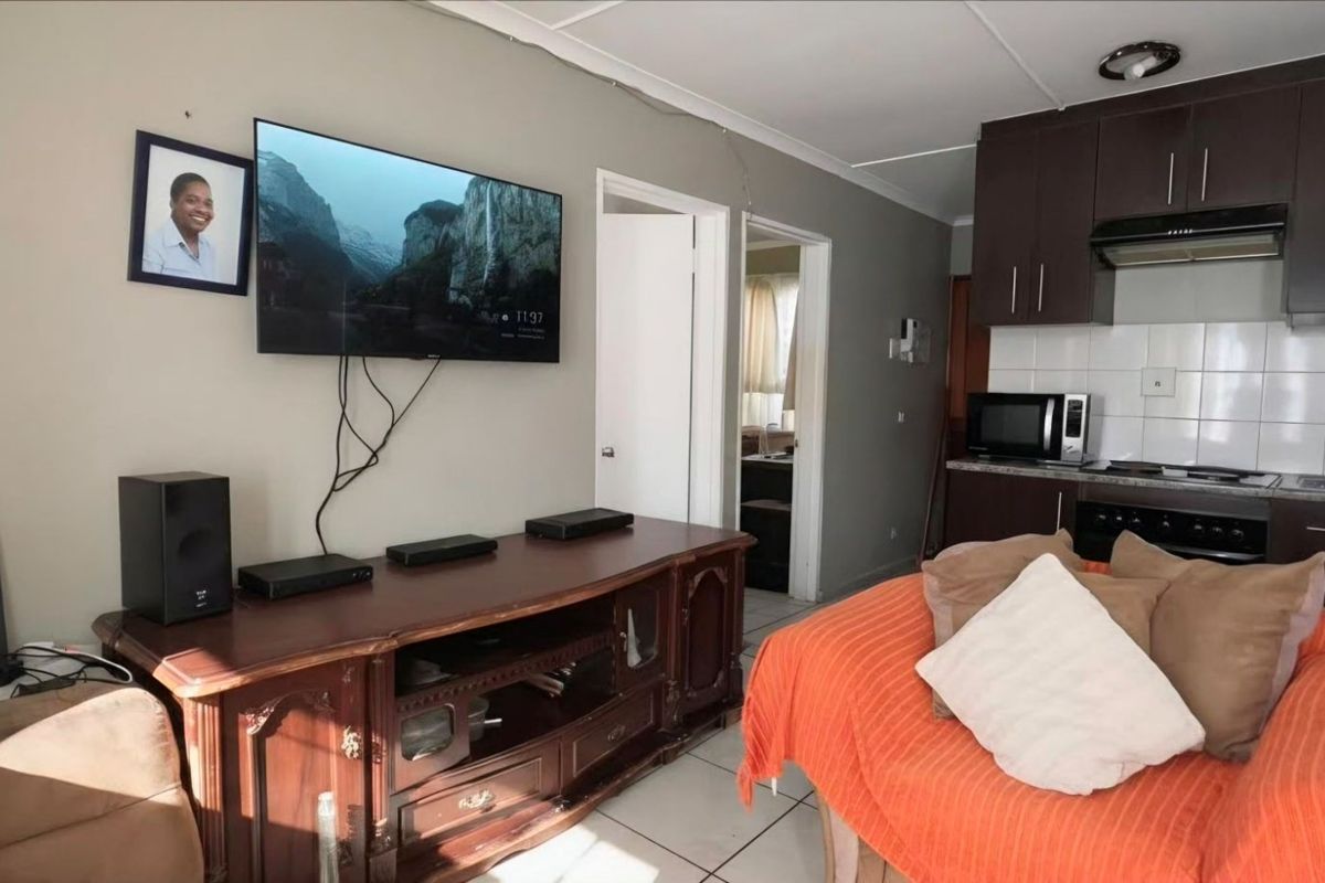 An open-plan living area featuring a compact kitchen with dark cabinetry, tiled flooring, and direct access to adjacent rooms.