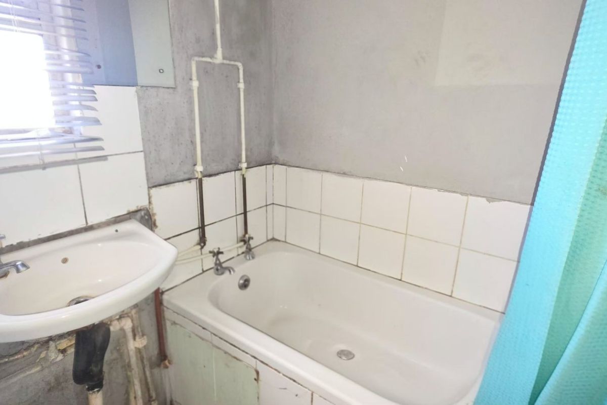A dated bathroom featuring a standard bathtub and wall-mounted basin with exposed plumbing and unfinished wall finishes requiring renovation.