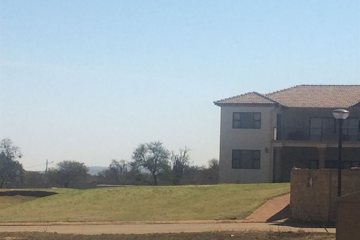 A view of a vacant residential plot with a paved driveway, boundary wall, and street lighting, adjacent to an existing two-story dwelling.