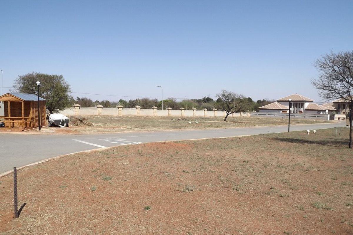 A vacant residential plot featuring a perimeter wall, paved road access, and a small wooden structure on site.