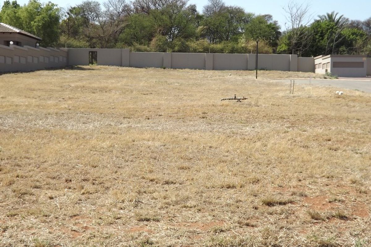 A vacant residential plot featuring dry grass, enclosed by a perimeter wall, offering a clear space for potential development.