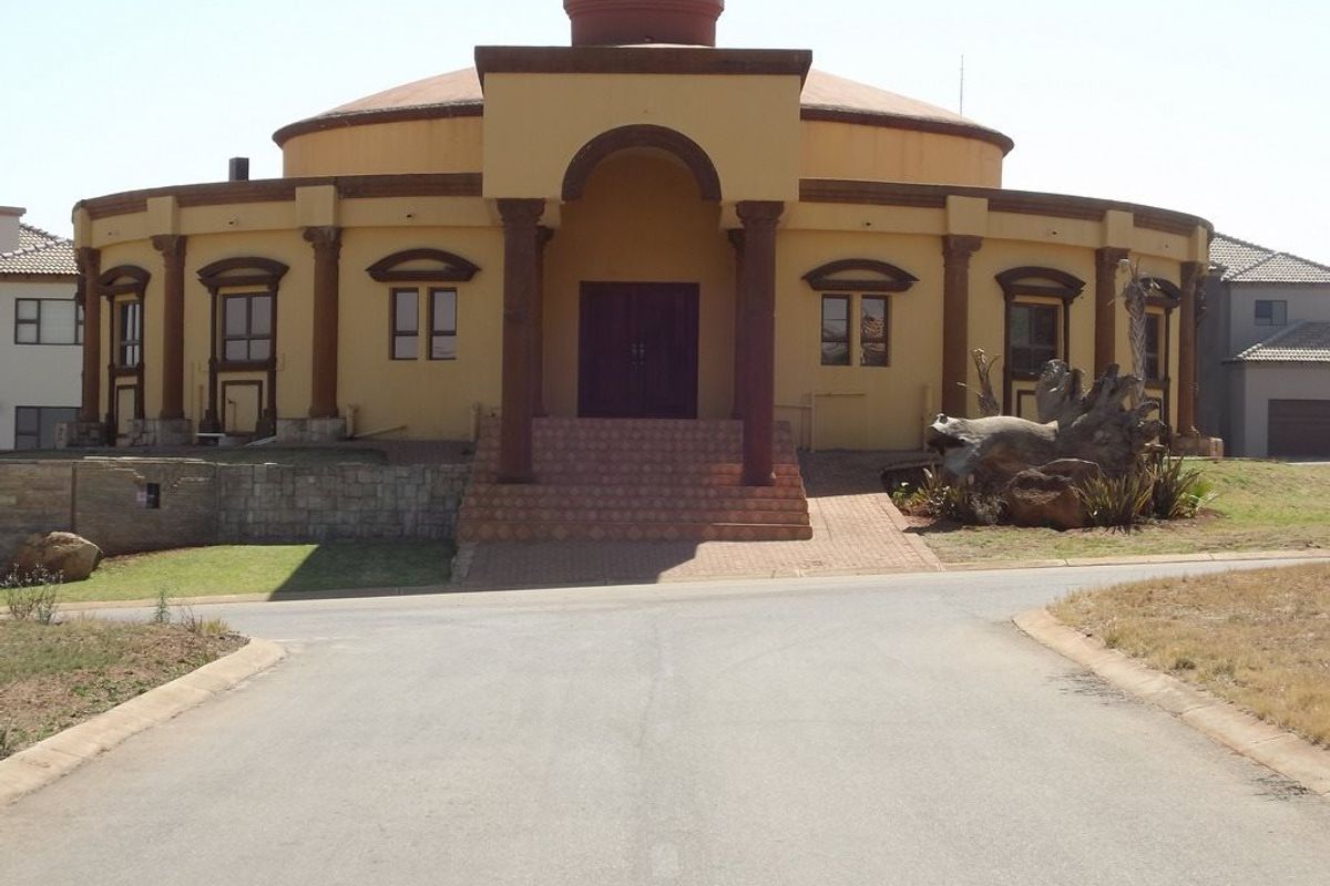 A unique circular residential property featuring a prominent arched entrance, decorative columns, and a paved driveway approach.