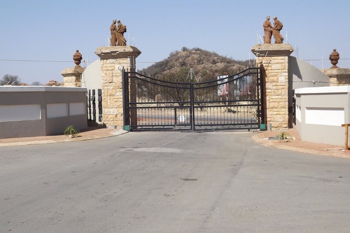 A secure gated entrance featuring stone-clad pillars, decorative statues, and wrought iron gates, providing a formal access point to the residential property.