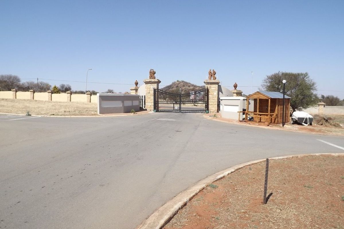 View of the secure gated entrance to the residential estate, featuring stone pillars, perimeter walling, and a guard house.