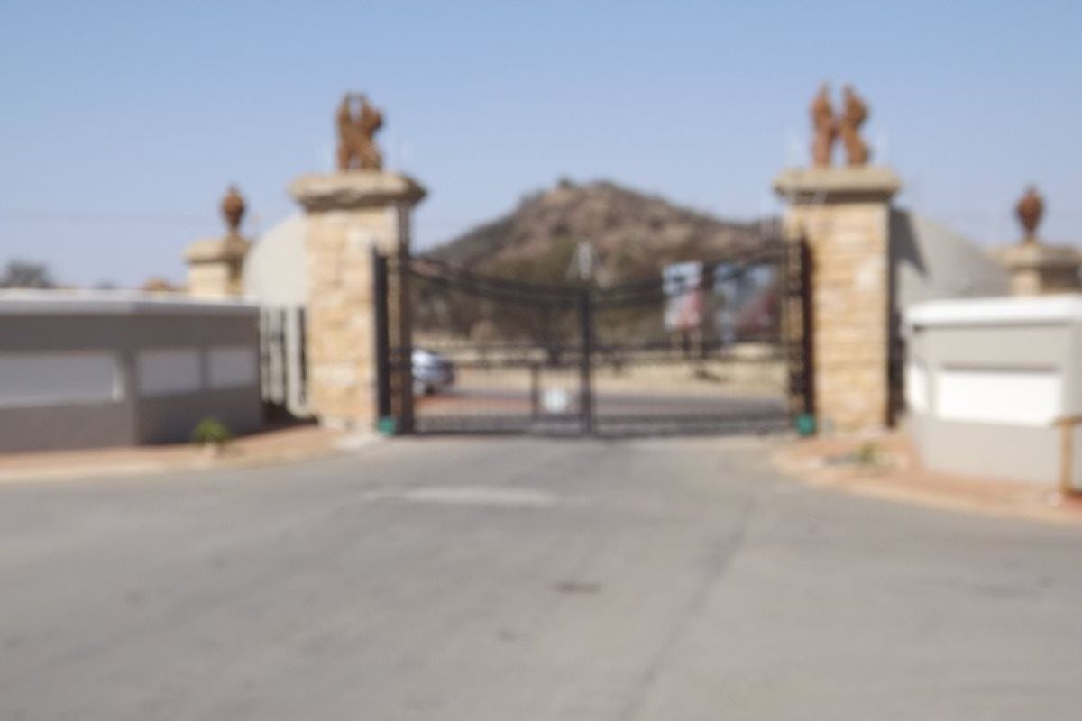 A view of the gated entrance to the residential property, featuring stone pillars and a paved driveway approach.