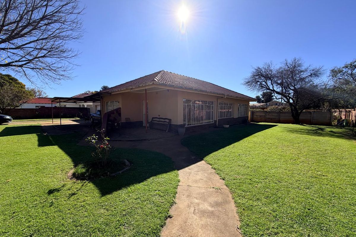 Rear view of the house featuring a tiled roof, covered patio area, and a spacious garden with a concrete pathway.