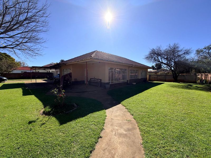 Rear view of the house featuring a tiled roof, covered patio area, and a spacious garden with a concrete pathway.