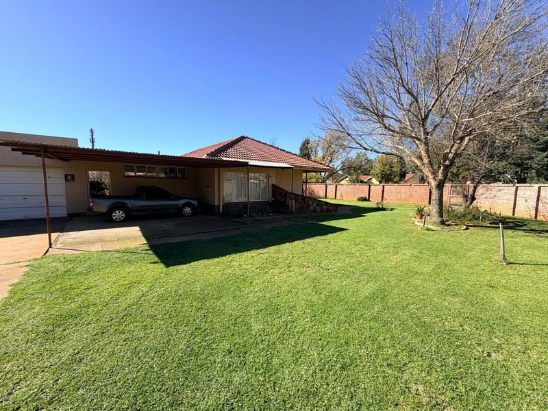 Rear view of the property featuring a spacious lawn, brick boundary wall, and a covered carport area.