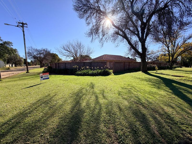 A wide-angle view of the property exterior featuring a large front lawn, brick boundary wall, and tiled roof structure.