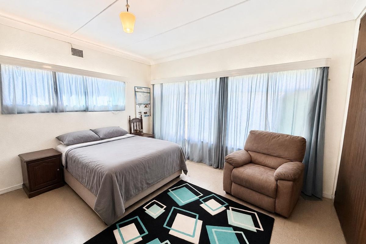 A spacious bedroom featuring large windows with curtains, a built-in wardrobe, and a ceiling light fixture.