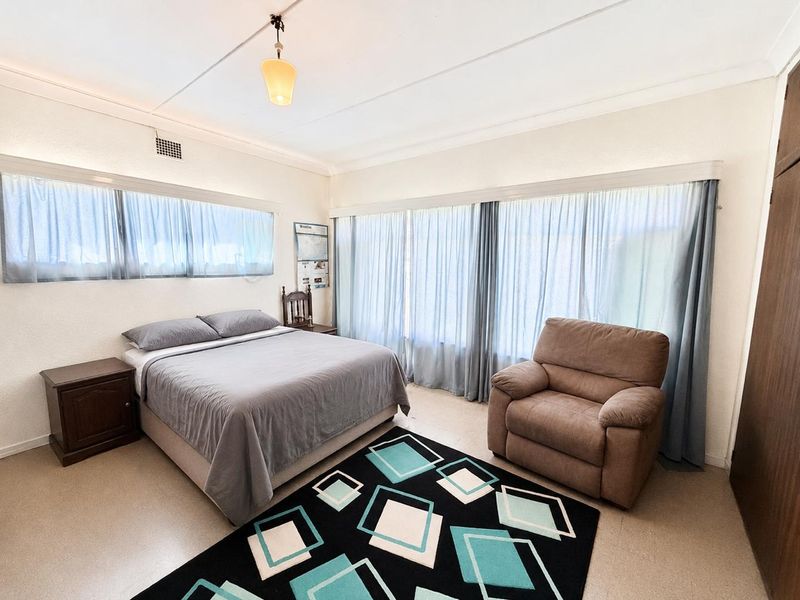 A spacious bedroom featuring large windows with curtains, a built-in wardrobe, and a ceiling light fixture.