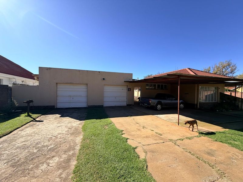 Front exterior view featuring a double garage, attached carport, and concrete driveway with established lawn area.