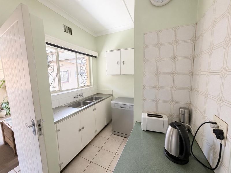 A functional scullery area featuring a double stainless steel sink, fitted cabinetry, and tiled splashbacks, providing practical utility space for the home.