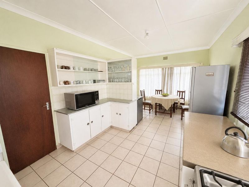 A functional kitchen featuring white built-in cabinetry, tiled flooring, and ample counter space, with an adjacent dining area.