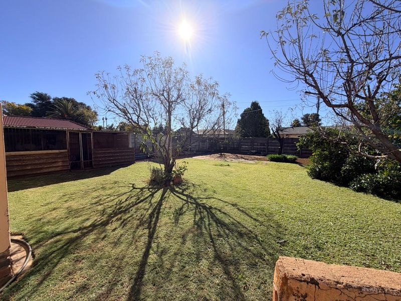 A spacious backyard featuring a large lawn, mature trees, and a precast concrete boundary wall, providing a private outdoor area.