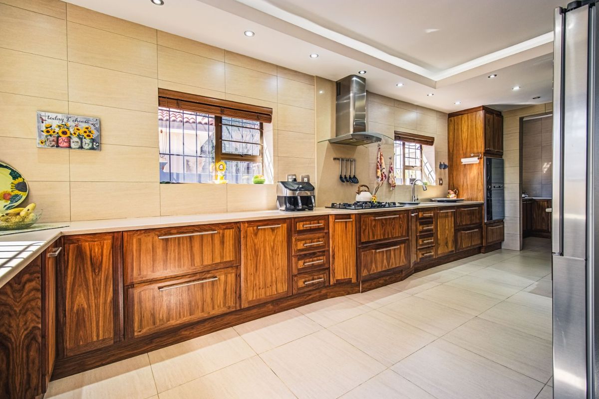 Modern kitchen featuring rich wooden cabinetry, stone countertops, integrated stainless steel appliances, and recessed ceiling lighting with neutral tiled finishes.