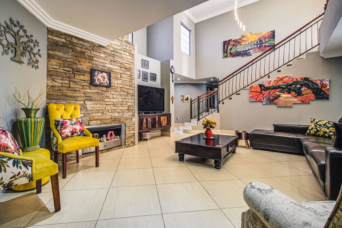 Spacious double-volume living room featuring a striking stone fireplace wall, tiled flooring, and an elegant staircase with metal balustrades.