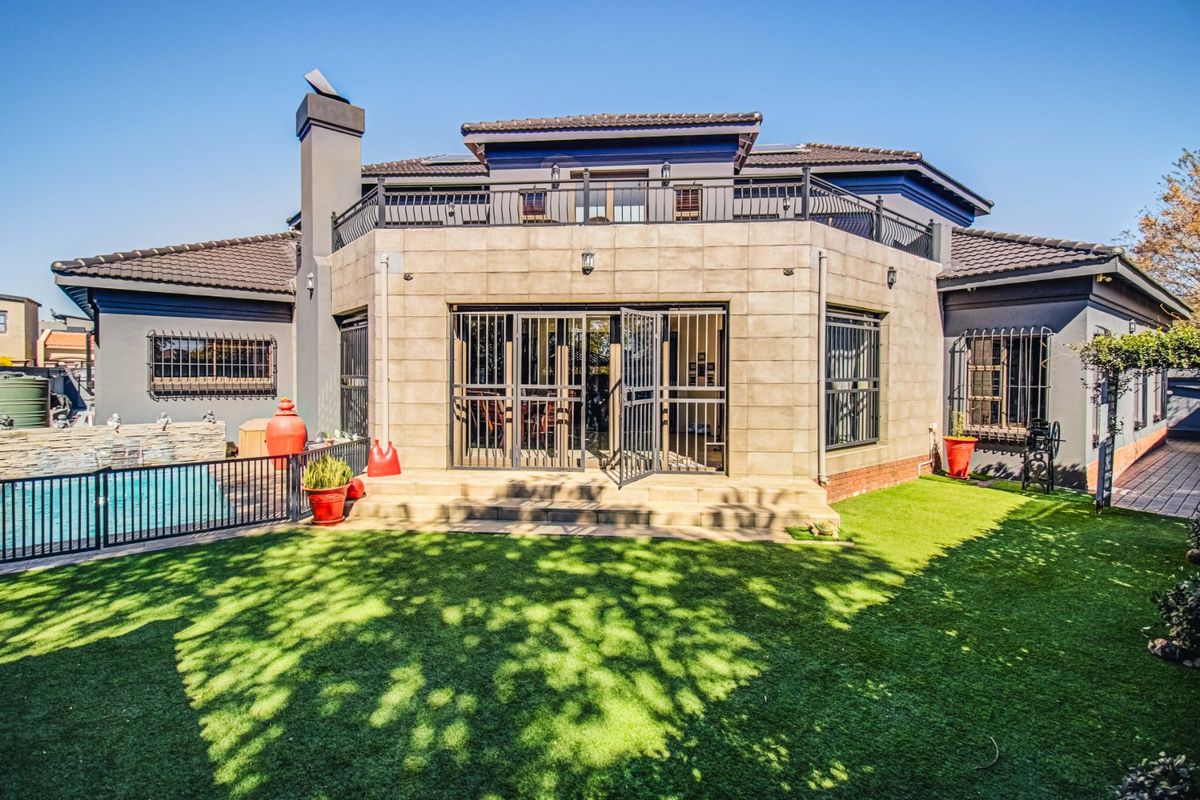 Rear view of the property featuring a tiled facade, balcony, swimming pool, and well-maintained artificial lawn area.