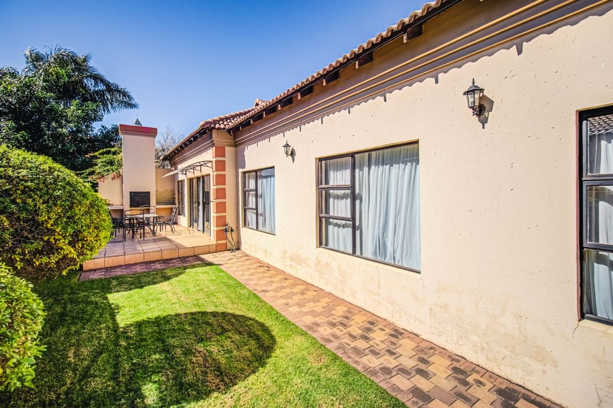 Rear exterior view featuring a paved walkway, a tiled patio area with a built-in braai, and well-maintained garden space.