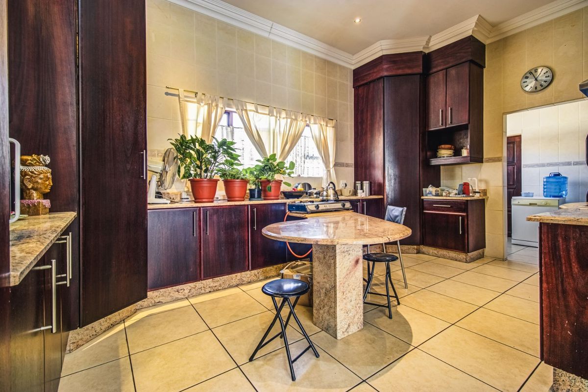 A functional kitchen featuring dark wood cabinetry, granite countertops, a central breakfast island, and tiled flooring with a neutral backsplash.