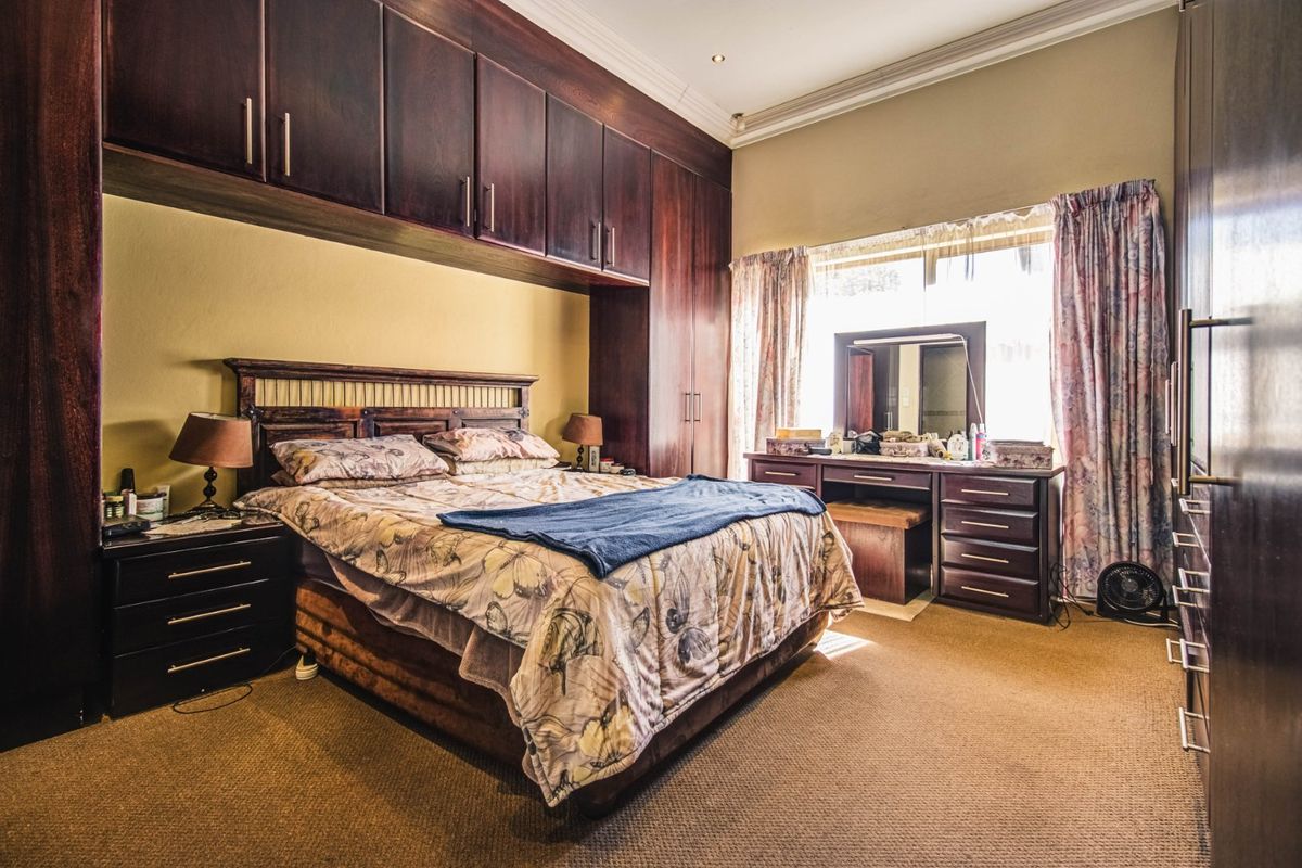 A spacious bedroom featuring extensive dark wood built-in cabinetry, recessed ceiling lighting, and carpeted flooring, offering ample storage and a functional layout.