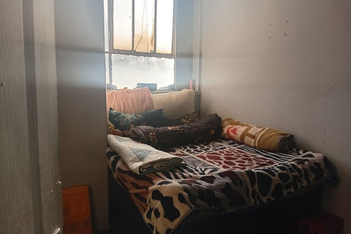 A compact bedroom featuring a multi-pane window, requiring cosmetic updates to the wall finishes and window frame to improve the overall living environment.