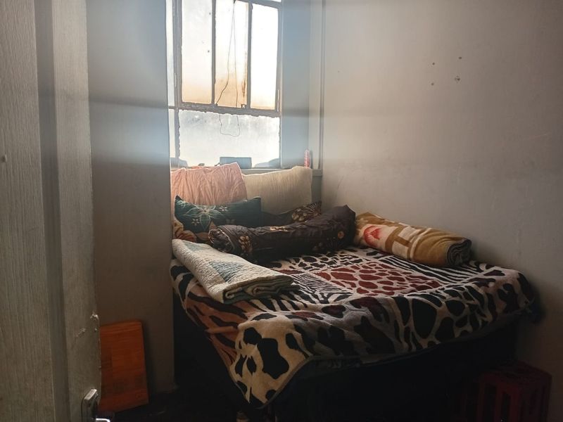 A compact bedroom featuring a multi-pane window, requiring cosmetic updates to the wall finishes and window frame to improve the overall living environment.