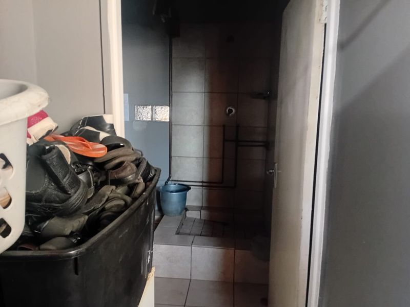 A small bathroom featuring a tiled shower enclosure with visible plumbing pipes and tiled flooring.
