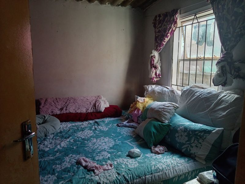 A small bedroom featuring a window with security bars and visible wear on the walls and ceiling, requiring cosmetic updates.