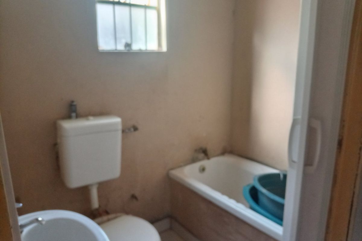 A dated bathroom featuring a standard bathtub, toilet, and basin, requiring significant cosmetic updates and refurbishment to improve its overall condition and appeal.