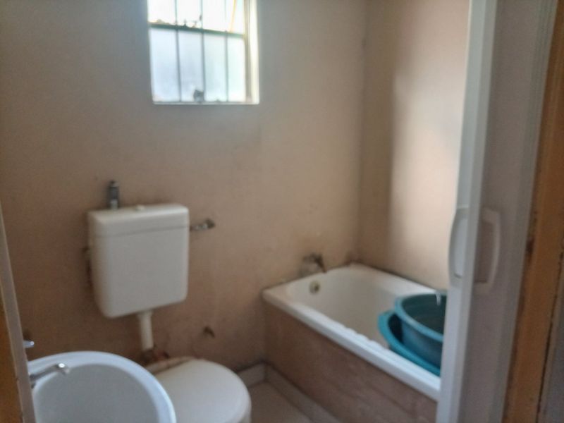 A dated bathroom featuring a standard bathtub, toilet, and basin, requiring significant cosmetic updates and refurbishment to improve its overall condition and appeal.
