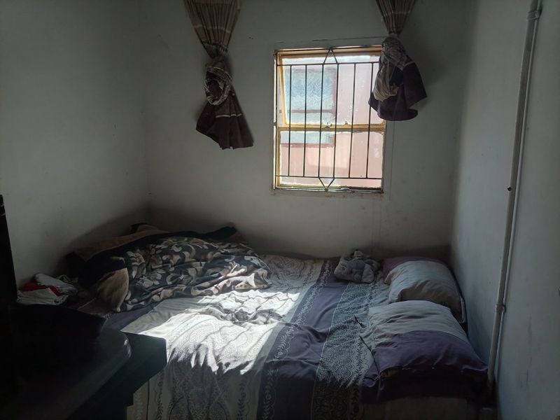A small bedroom featuring a window with security bars, requiring cosmetic updates and wall repairs to improve the overall condition.