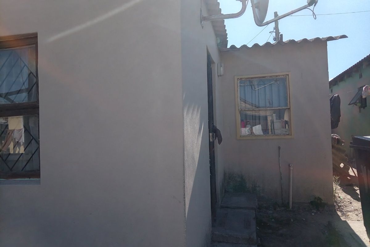 Rear exterior view of the property showing basic masonry construction, security bars on windows, and a satellite dish installation.