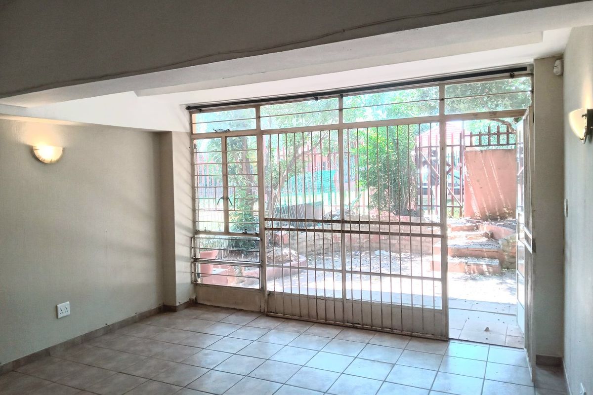 An empty living room featuring tiled flooring, wall-mounted lighting, and a large sliding glass door with a security gate leading to an outdoor area.
