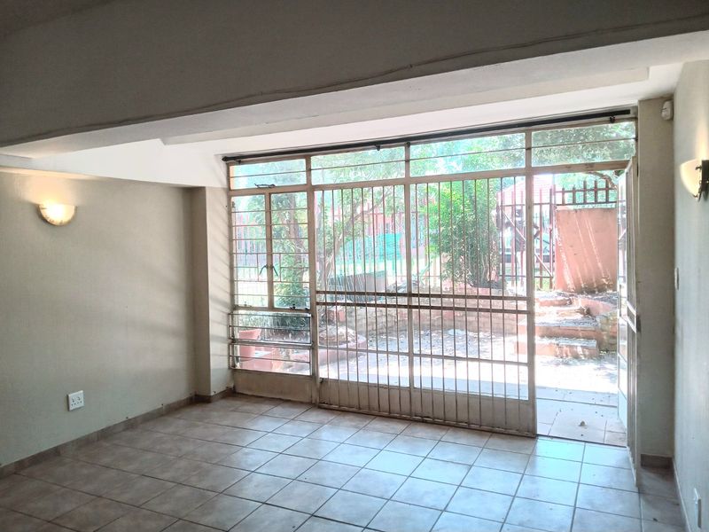 An empty living room featuring tiled flooring, wall-mounted lighting, and a large sliding glass door with a security gate leading to an outdoor area.