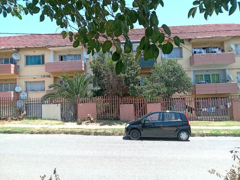 Front elevation of a multi-story apartment complex featuring tiled roofing, private balconies, and secure perimeter fencing with a street-facing facade.